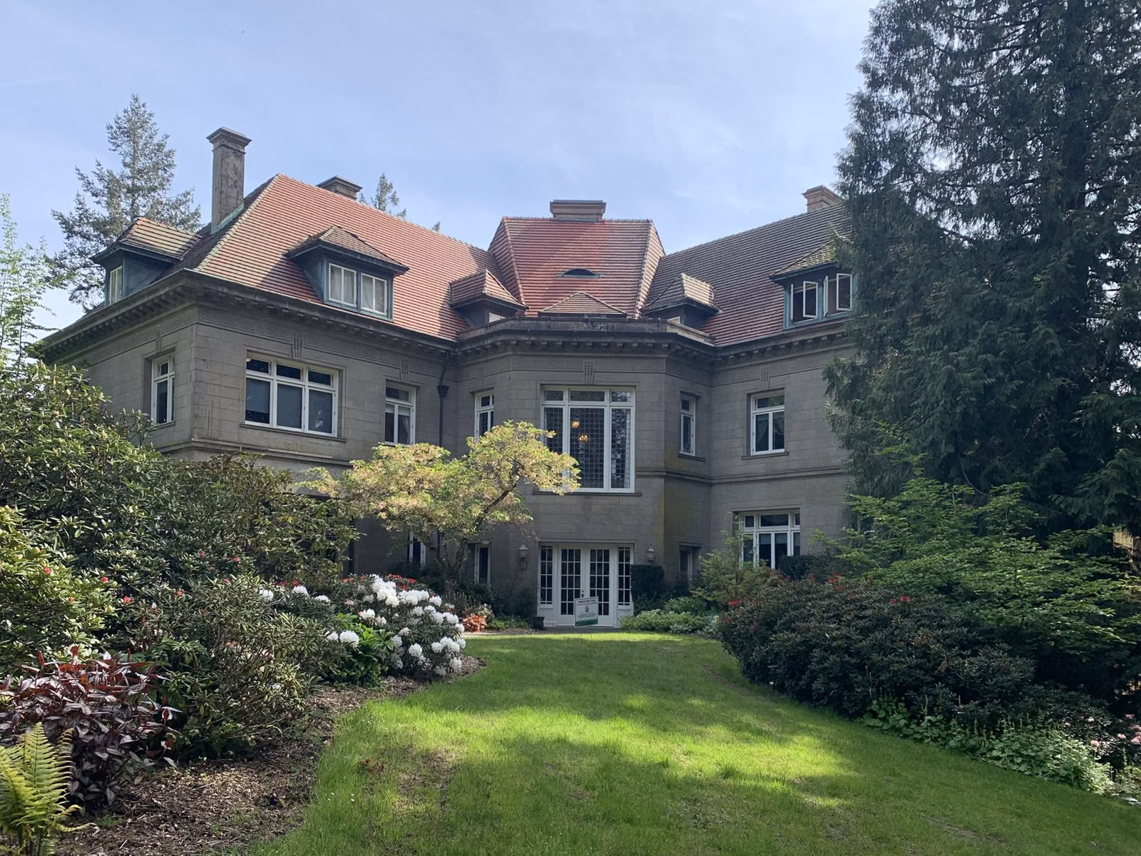 Pittock Mansion, a stone house with red tile roofs, seen across its rear lawn and gardens in Portland